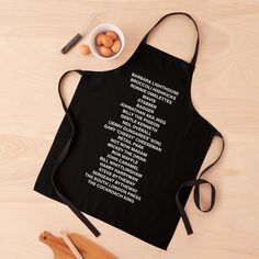 a black apron with words on it sitting next to some wooden spoons and eggs