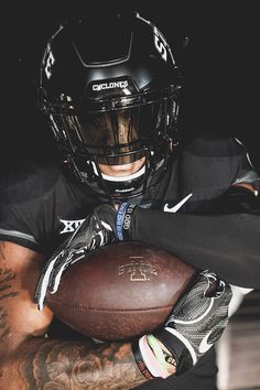 a man holding a football in his right hand and wearing a black uniform with white lettering on it