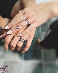 two people holding each other's hands with tattoos on their fingers and one has a heart