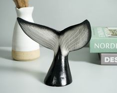 a white and black whale tail vase next to two books