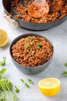 two pans filled with baked beans and garnished with parsley next to lemon wedges