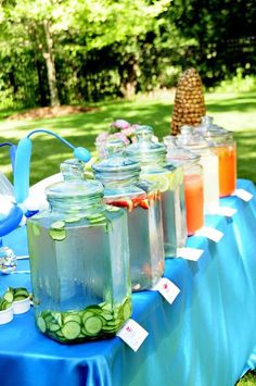 several jars with cucumbers in them sitting on a blue table cloth at an outdoor party