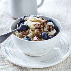 a bowl filled with fruit and nuts on top of a white plate next to a cup