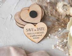 wooden save the date magnets with hearts on them and dried flowers in the background