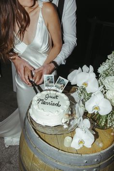 a bride and groom cutting their wedding cake with an old fashioned barrel as the backdrop