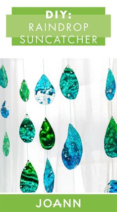 a green and blue wind catcher hanging from the side of a window with raindrops painted on it