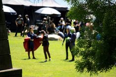 some people are standing in the grass and one is holding a red cape while others stand around