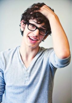 a young man wearing glasses is smiling and holding his head with one hand while looking at the camera