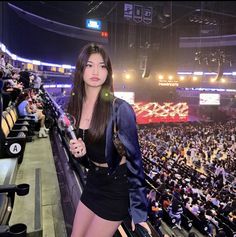 a woman standing in front of an audience at a sporting event, holding a microphone