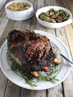 a large piece of meat sitting on top of a white plate next to bowls of food