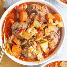 two bowls filled with meat and vegetable stew on top of a table next to silverware