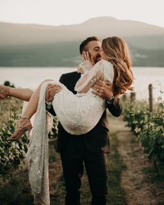 a man holding a woman in his arms while standing next to a field with flowers