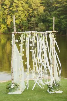 an outdoor wedding ceremony setup with white flowers and ribbons hanging from the back of it