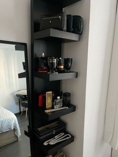 there is a black shelf with many items on it in the corner next to a mirror