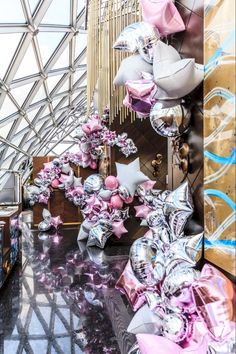 balloons and streamers are hanging from the ceiling in a building that is filled with pink and silver decorations