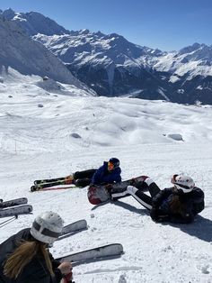 people sitting in the snow with skis on their feet and mountains in the background