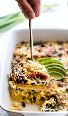 a person dipping an avocado into a casserole dish with cheese and other toppings