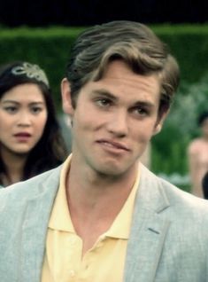 a man in a suit and yellow shirt standing next to a woman wearing a tiara