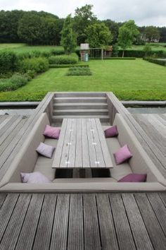 a wooden deck with benches and purple pillows on the back side, overlooking a grassy area