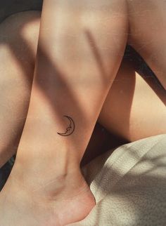 a woman's foot with a small crescent tattoo on her left ankle and the moon behind it