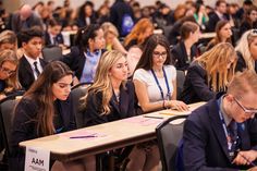 many people are sitting at desks in a room full of students and one person is taking notes