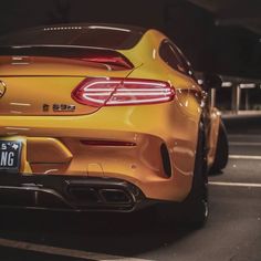 the rear end of a yellow mercedes sls parked in a parking lot at night