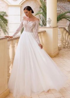 a woman in a white wedding dress standing on a balcony with palm trees behind her