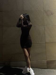 a woman standing in front of a wall with her hands on her head and looking at the ground