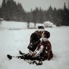 two people sitting in the snow kissing each other