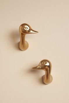 two brass colored ducks are standing next to each other on a white surface, one is facing the opposite direction