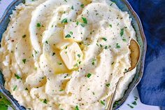 mashed potatoes with parsley in a blue bowl on a white tablecloth and silver spoon