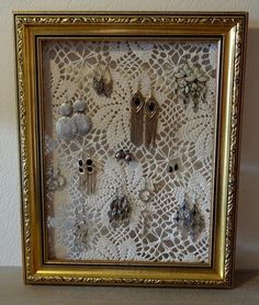 a gold frame with several pairs of earrings in it on a white table top next to a wall