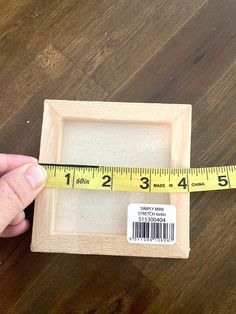 a person holding a measuring tape near a wooden frame on a wood floor with a ruler in front of it