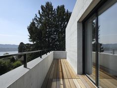 a balcony with wooden flooring next to a white wall and trees in the background