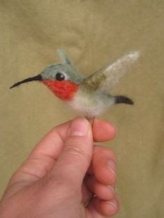 a hand is holding a tiny bird made out of wool and needled with thread