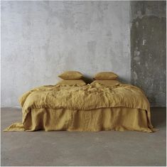 a bed with two pillows on top of it in front of a concrete wall and floor