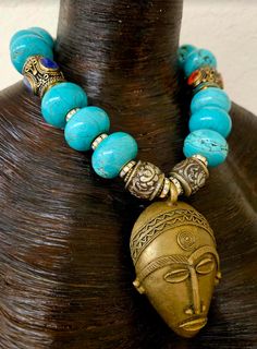 A 4" x 2.5" detailed African lost wax brass mask is the focal point on this robin's egg blue, faux turquoise magnesite rondelle tribal beaded necklace. Flanking the pendant are four rhinestone rondelles and two ornate Tibetan repousse beads. Measuring a non-adjustable 20", this bold, chunky and somewhat heavy statement piece features two very ornate hand crafted Tibetan tribal drum beads with inlaid lapis lazuli and coral. Separating the blue rondelles are golden aurora borealis rhinestone ronde One Of A Kind Blue Turquoise Necklace For Festival, Traditional Blue Patina Necklace, Traditional Blue Turquoise Necklace With Patina, Blue Turquoise Necklace For Festivals, Traditional Turquoise Necklace With Patina, Robin's Egg Blue, Chest Piece, Metal Ball, Lost Wax