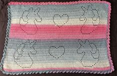 a crocheted pillow with pink, blue and white stripes on the bottom is laying on a brown surface