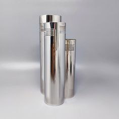 three stainless steel vases sitting side by side on a white surface, one is empty and the other has a straw sticking out of it