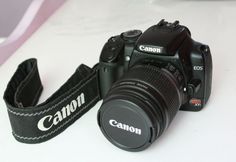 a canon camera sitting on top of a white table next to a black strap with the word canon printed on it