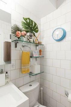 a white toilet sitting next to a bathroom sink under a clock mounted on a wall