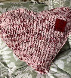 a knitted heart shaped pillow sitting on top of a bed