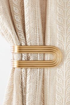 a pair of gold metal clips attached to the side of a beige curtain with white lace