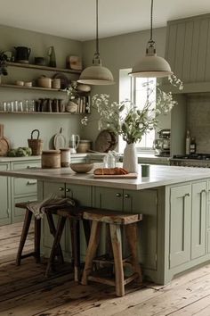 a kitchen with green cabinets and wooden flooring, two stools in front of the island