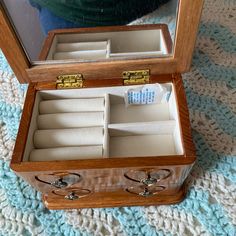 an open wooden box with jewelry inside sitting on a blue and white carpeted floor