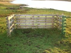 a wooden fence sitting on top of a lush green field next to a lake in the distance