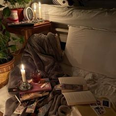 a pile of books sitting on top of a bed next to a candle and potted plant