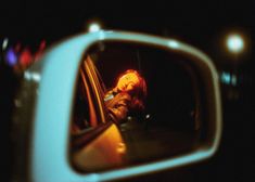 a rear view mirror with a reflection of a woman sitting in a car at night