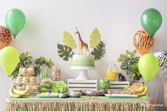 a table topped with lots of desserts and jungle themed balloons in front of a white wall