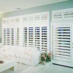 a living room filled with white furniture and windows covered in shutters on both sides